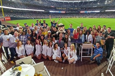 Group photo of TCWGlobal workers at the Templeton Rye Barrel Deck at Petco Park. The Padres mascot the Friar is in the middle of the photo