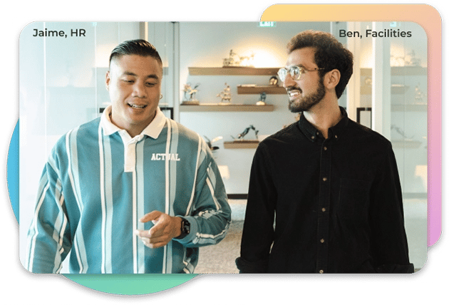 Two men having a conversation while walking towards the camera. The man on the left has a blue shirt with white stripes, and the man on the right has a black button up shirt with glasses on